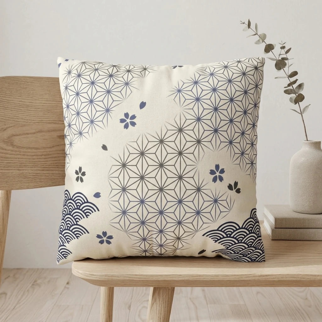 Cream cushion with blue Japanese wave and geometric patterns on a light wooden chair in a minimalist interior setting with books and a vase.