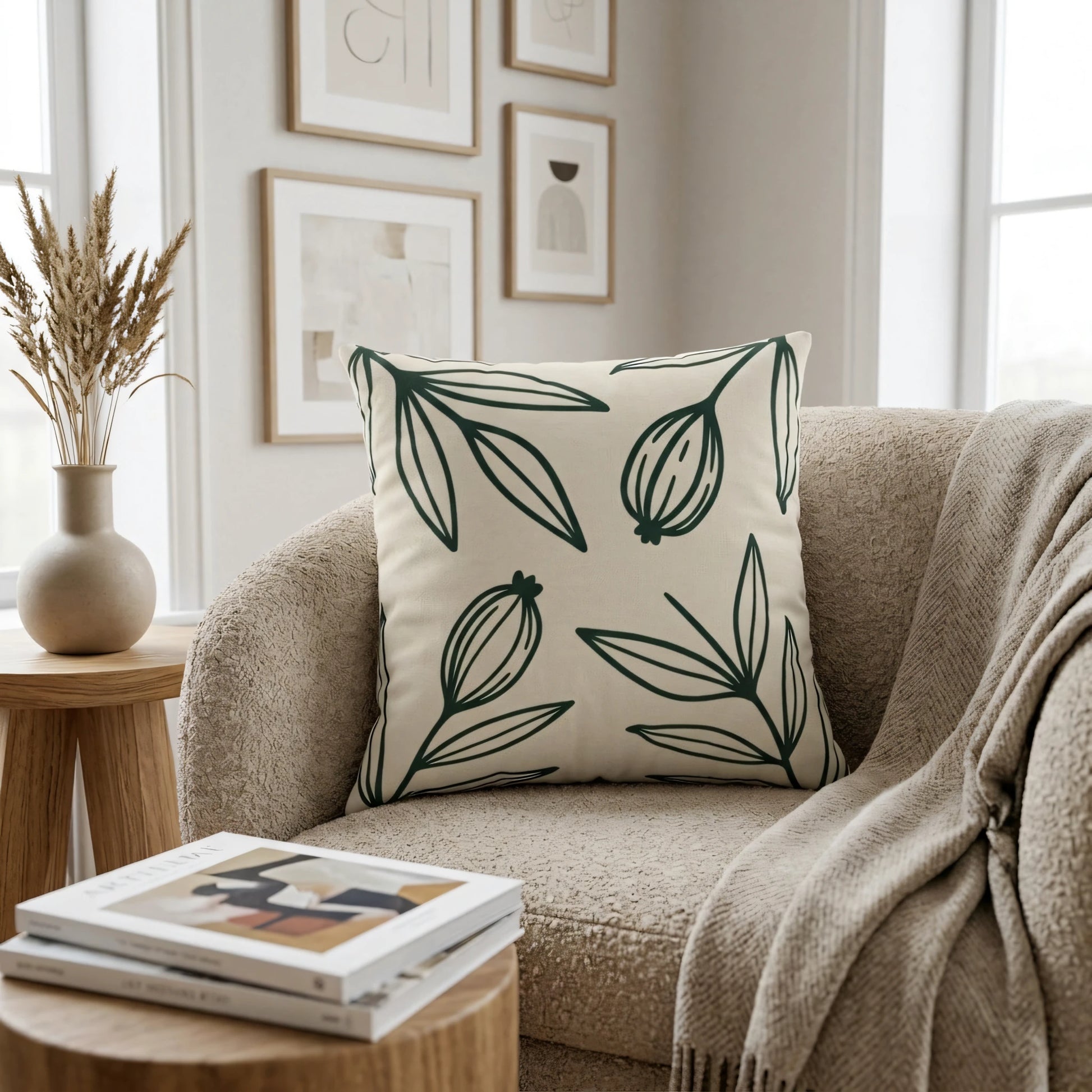 Minimalist cream throw pillow with dark green botanical leaf print on a bouclé armchair in a cozy neutral living room setting.