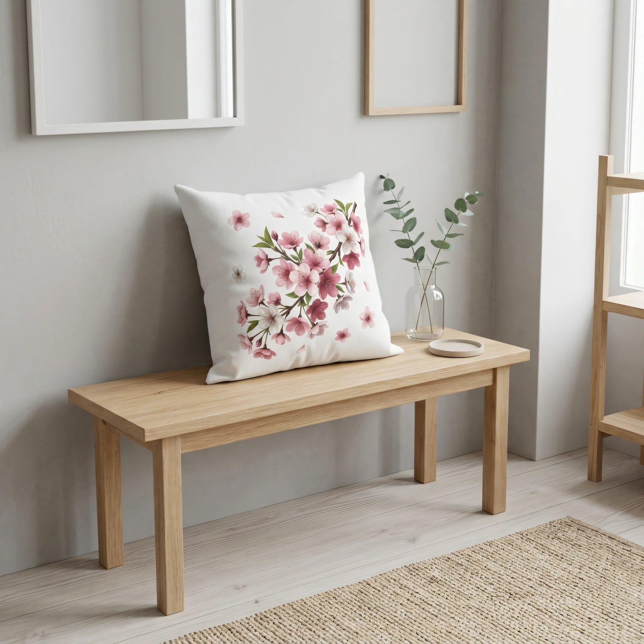 Decorative white throw pillow with pink floral cherry blossom design on a light wood bench in a bright, minimalist modern home setting.