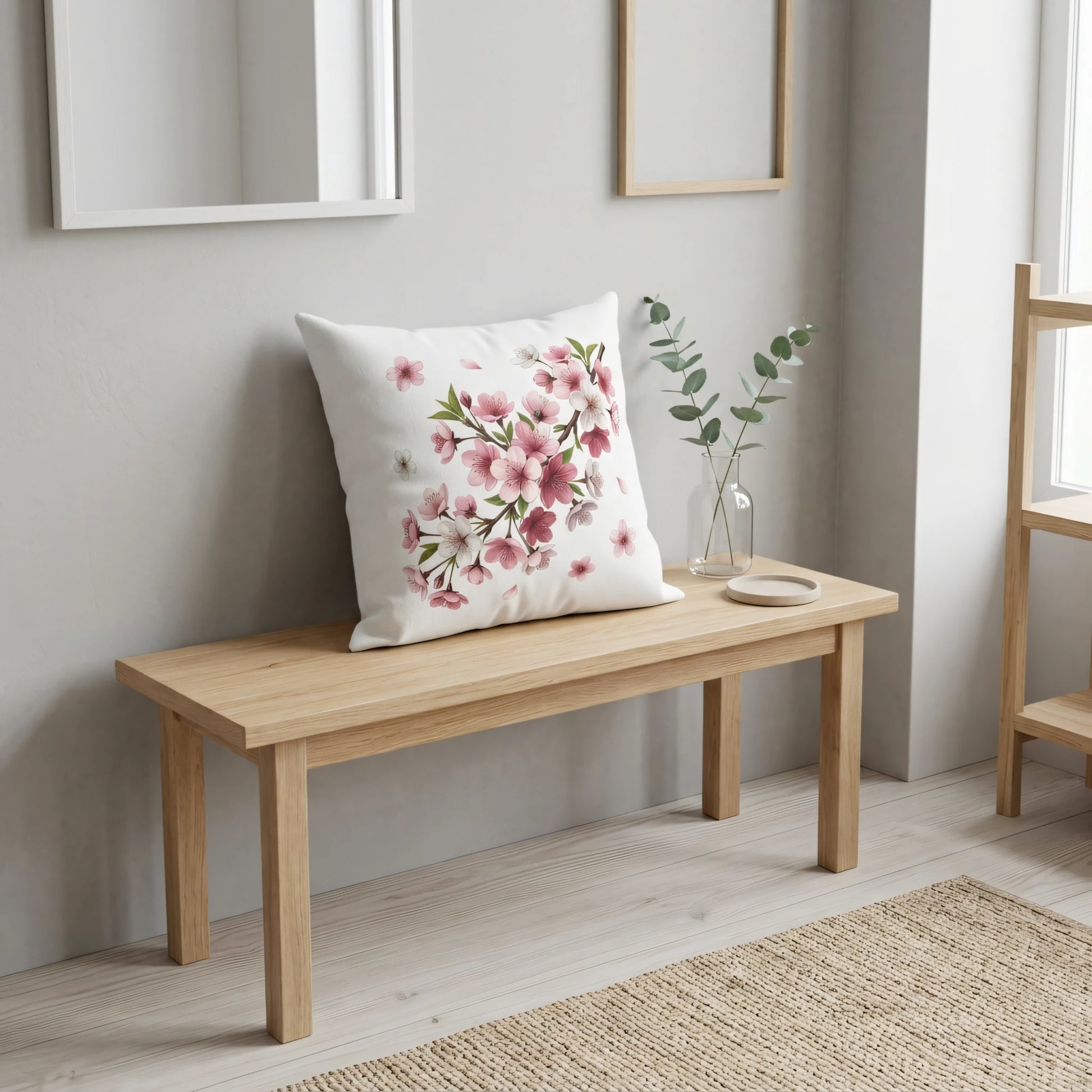 Decorative white throw pillow with pink floral cherry blossom design on a light wood bench in a bright, minimalist modern home setting.