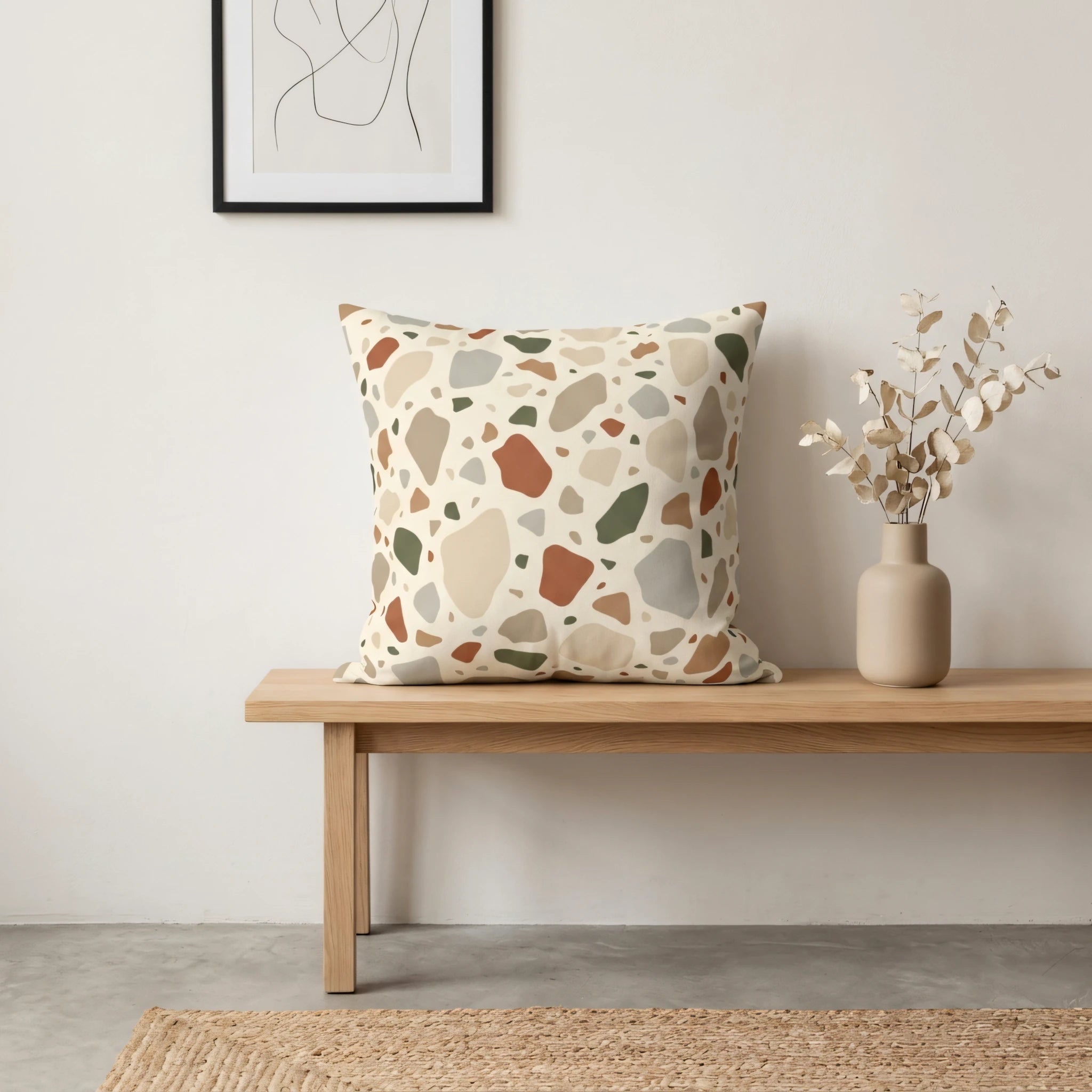 Square terrazzo pattern pillow in earthy colors on a light wood bench in a minimalist home interior with a neutral vase and framed art.