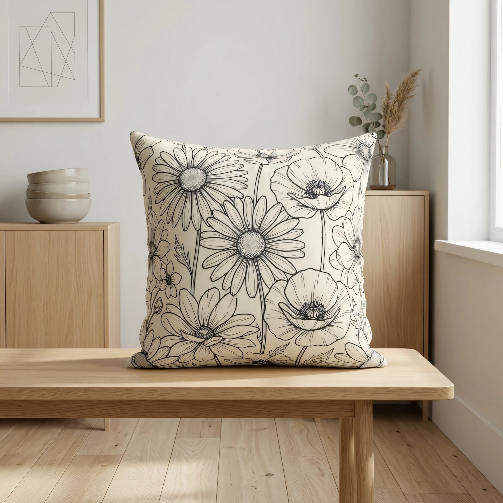 Decorative cushion with black floral line art pattern on a wooden bench in a minimalist interior setting with neutral decor and natural light.