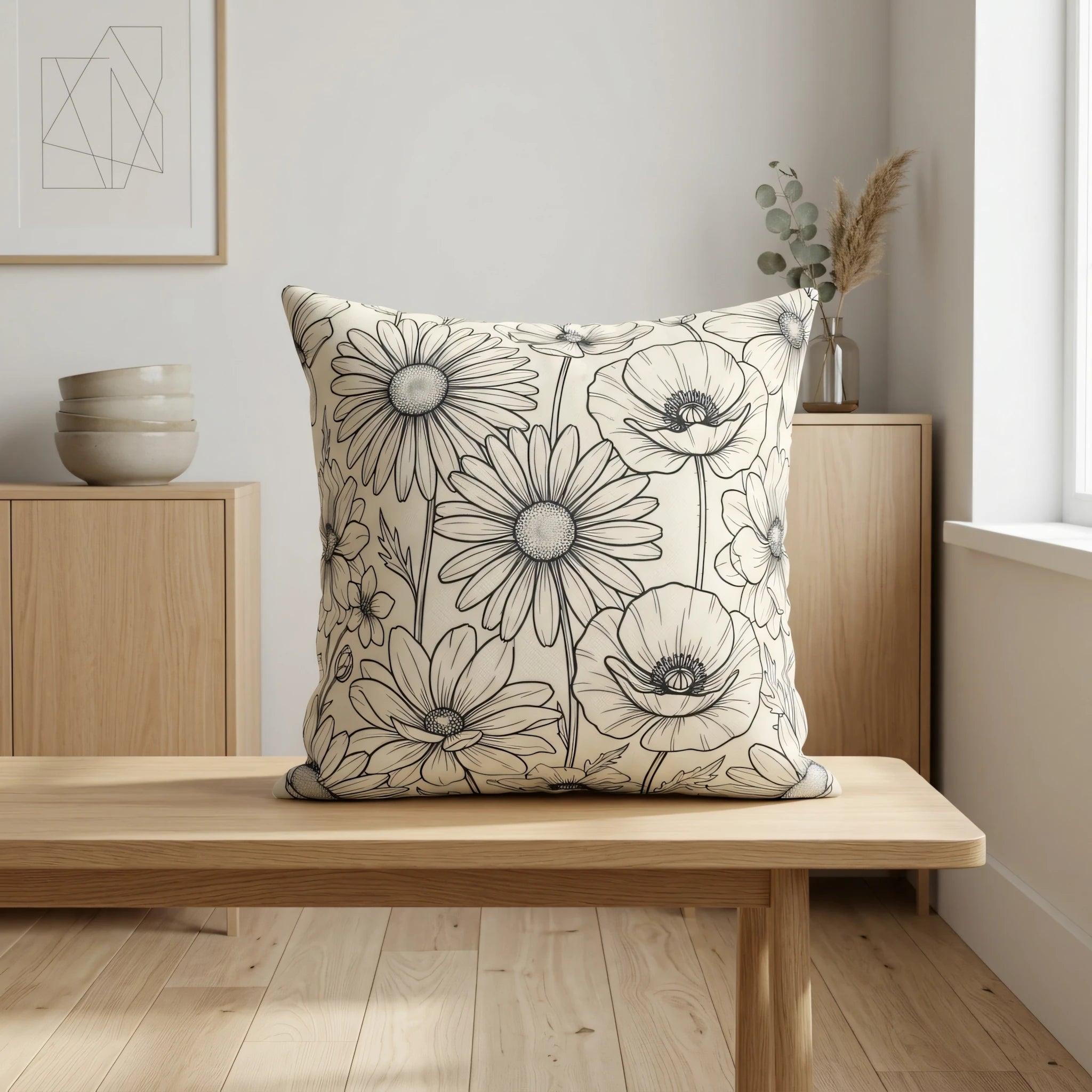 Decorative cushion with black floral line art pattern on a wooden bench in a minimalist interior setting with neutral decor and natural light.