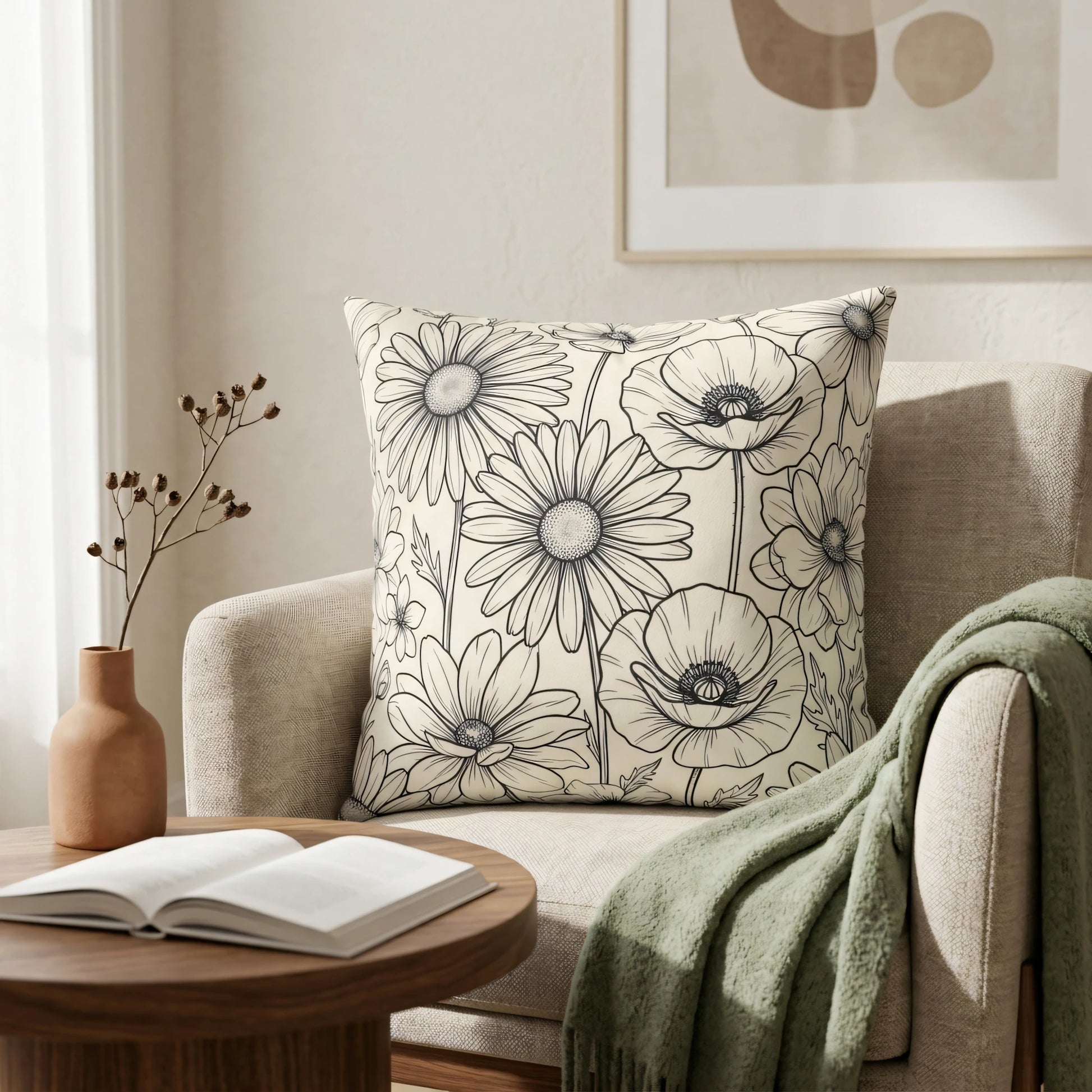 Black and white floral line art cushion on a beige armchair with a green throw and wooden side table in a cozy, bright living room.