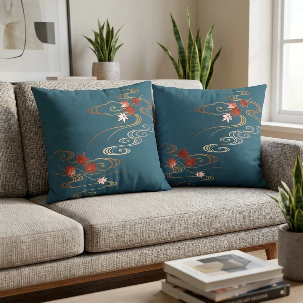 Two teal blue decorative cushions with Japanese red maple leaf patterns on a modern gray sofa in a bright living room setting.