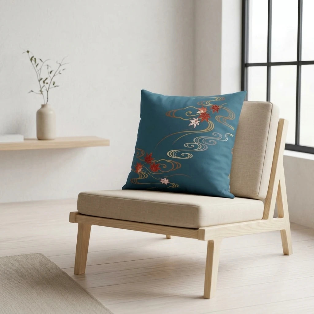 Teal pillow with Japanese maple leaves and gold water patterns on a wooden chair in a bright, minimalist interior lifestyle scene.