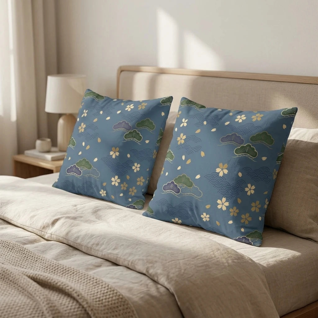 Two blue Japanese pattern pillows featuring cherry blossoms and pine trees on a beige bed in a sunlit bedroom lifestyle shot.