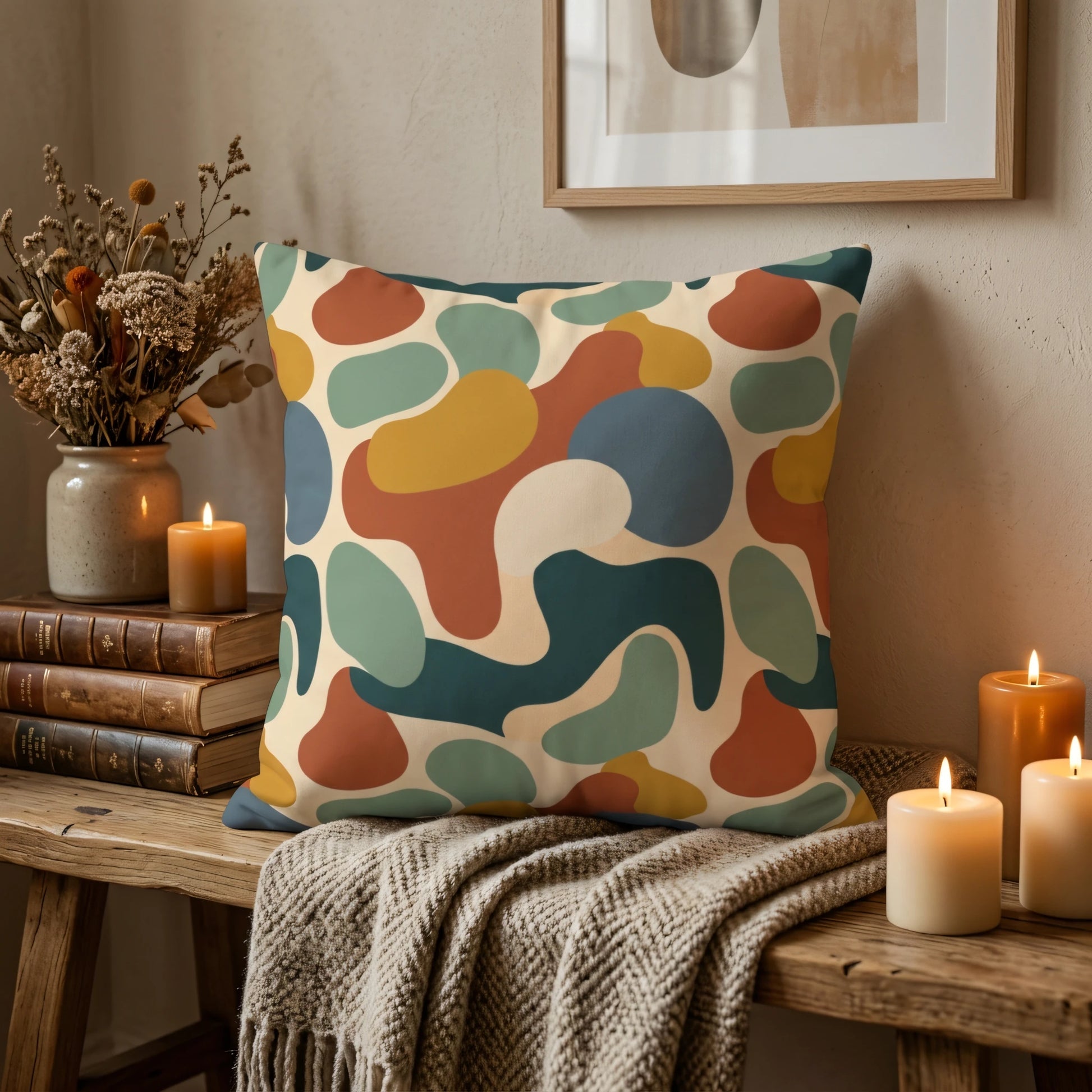 Abstract patterned cushion with organic shapes in rust, mustard, and teal, styled on a wooden bench with warm candles in a cozy home setting.
