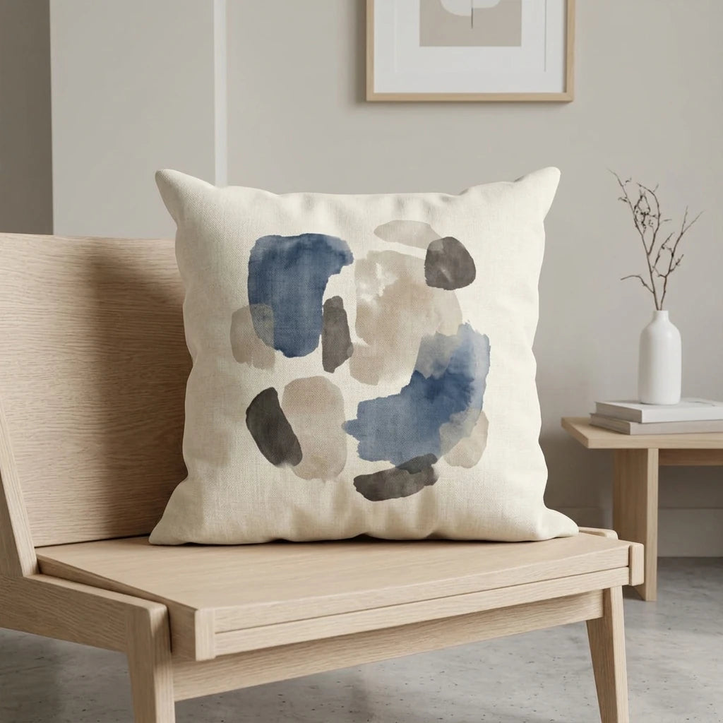Abstract navy and neutral watercolor throw pillow displayed on a wooden chair in a minimalist interior with a white vase and art.