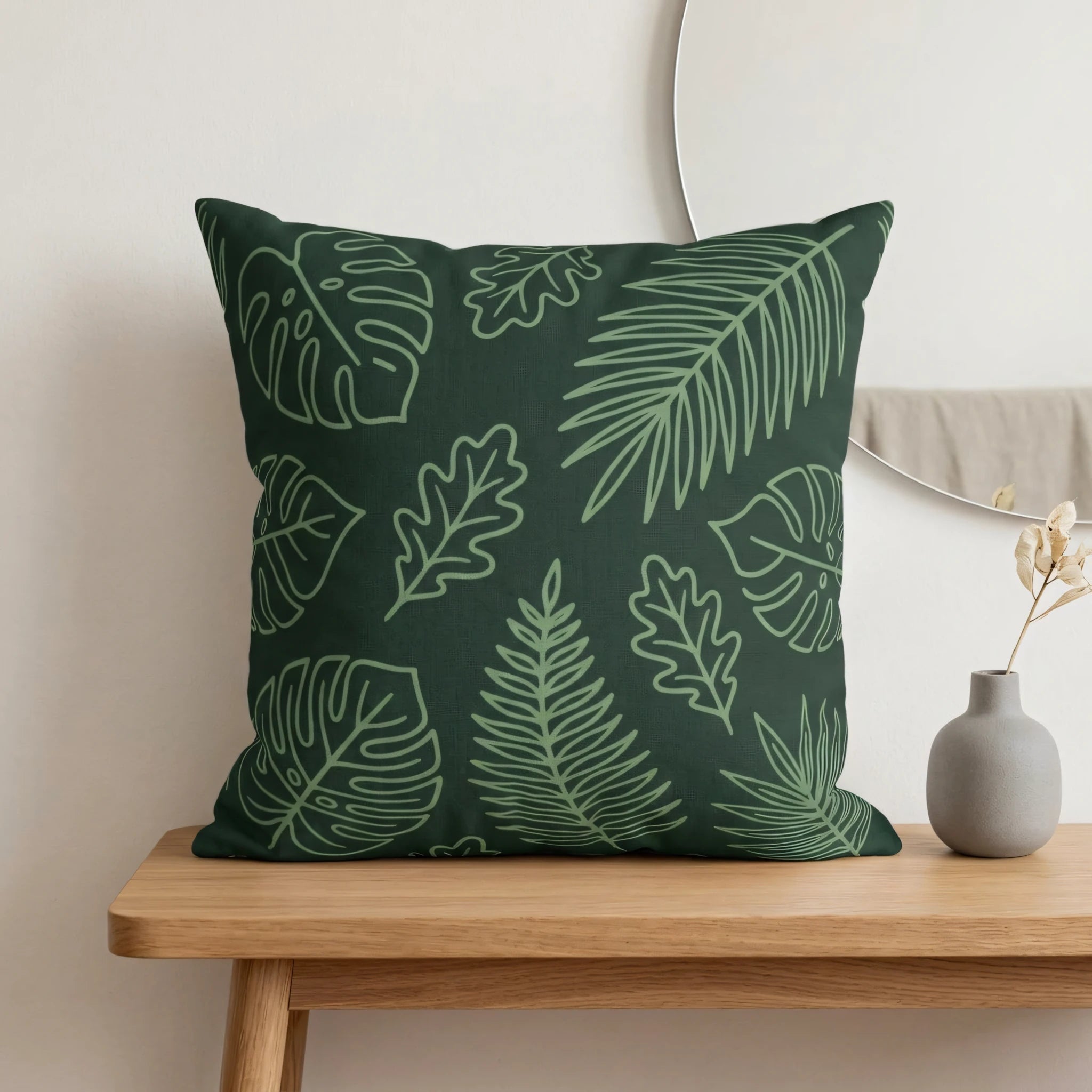 Green botanical leaf pattern throw pillow on a wooden table in a minimalist interior setting with a grey vase and mirror.