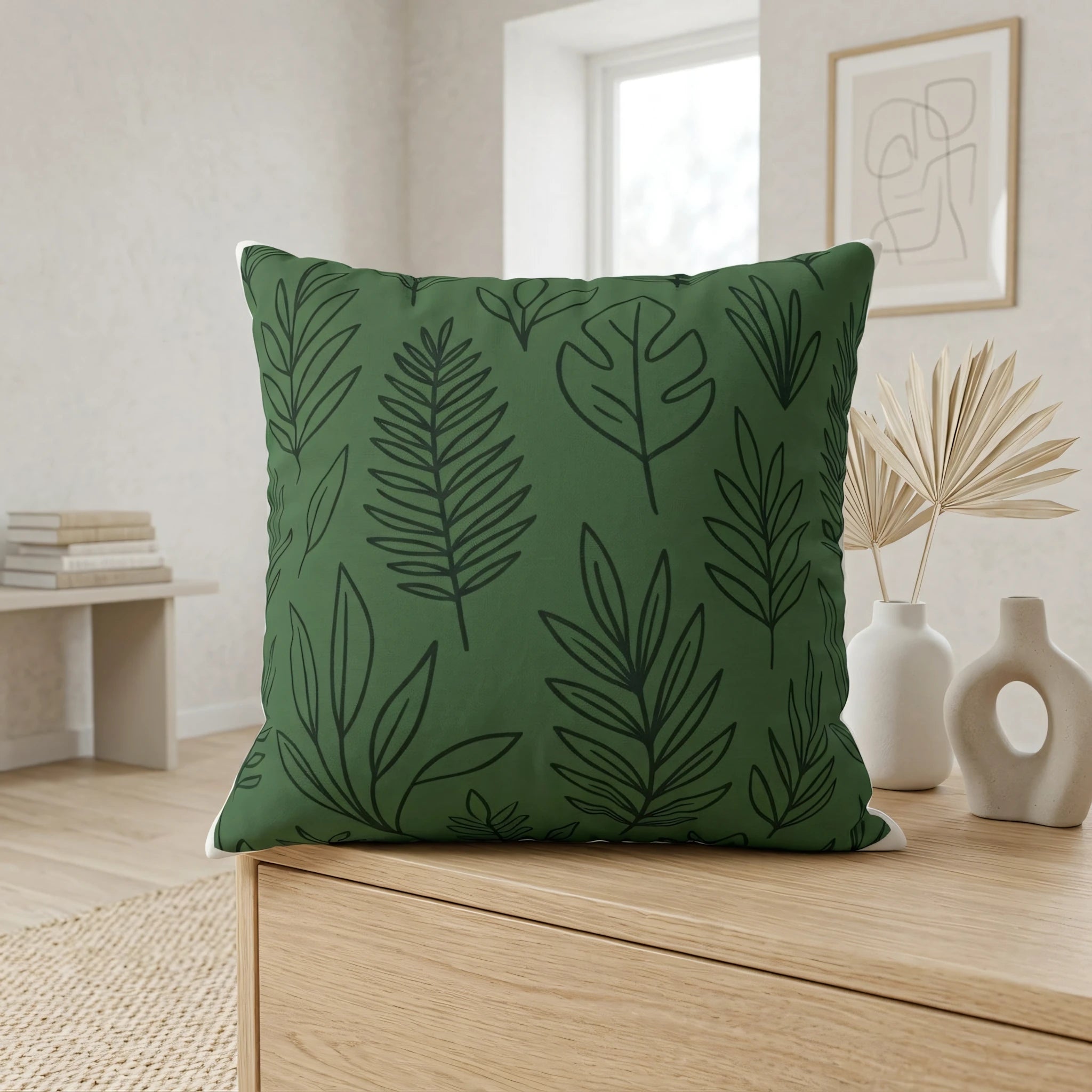 Green botanical throw pillow with black leaf patterns on a wooden cabinet in a minimalist home interior with white vases and dried palms.