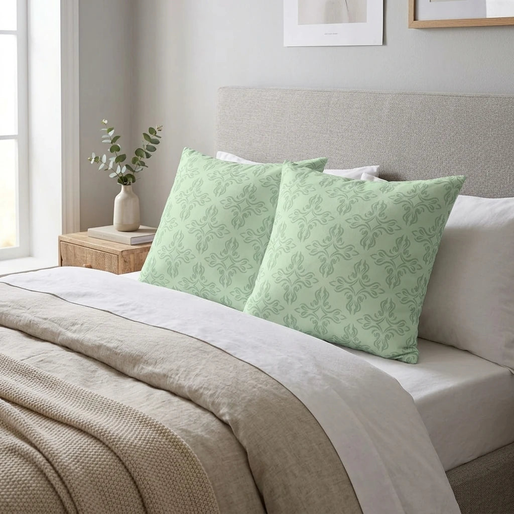 Sage green decorative throw pillows with a geometric damask pattern on a neutral bed, part of a cozy bedroom duo lifestyle scene.