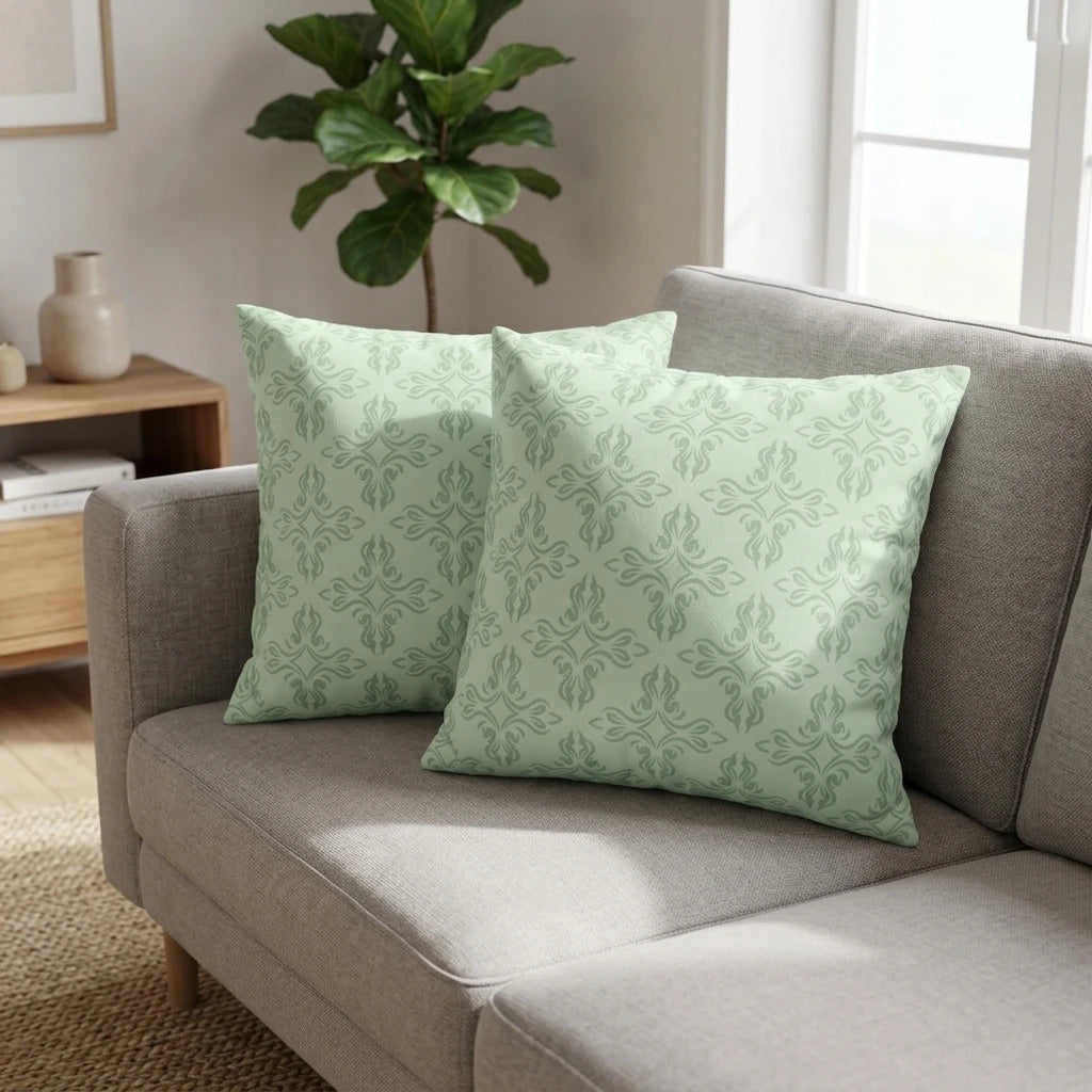 Pair of sage green pillows with a damask pattern on a grey couch in a modern living room setting.