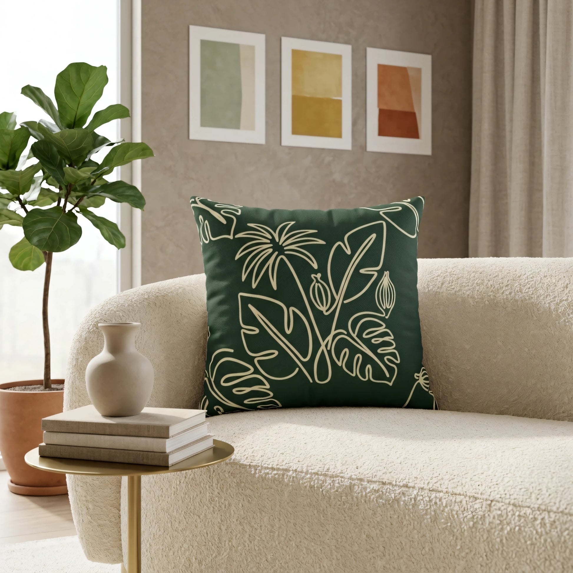Dark green tropical leaf pattern throw pillow on a cream textured sofa in a modern minimalist living room with a gold side table and indoor plant.