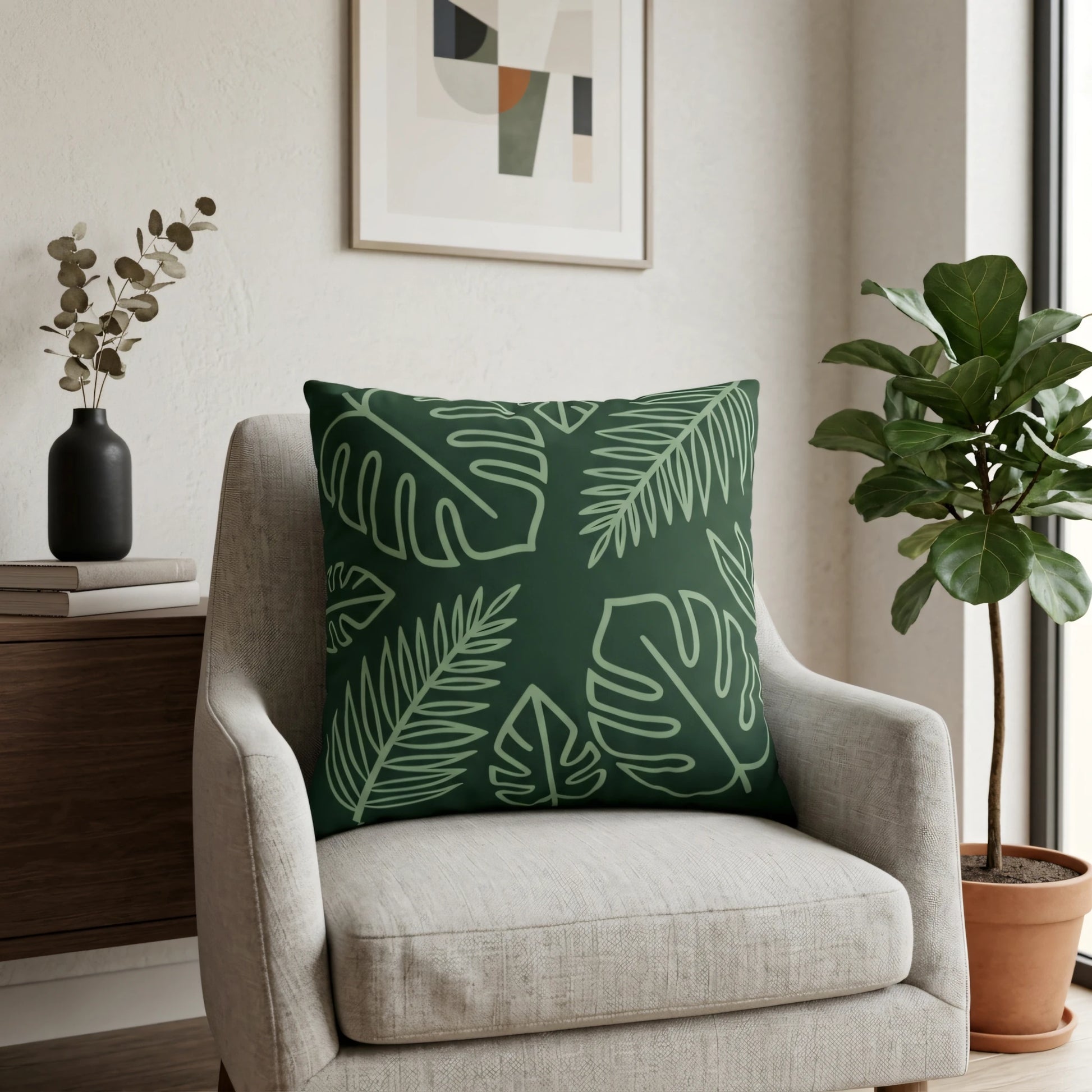 Dark green throw pillow with tropical leaf line art on a light gray armchair in a modern minimalist living room scene.