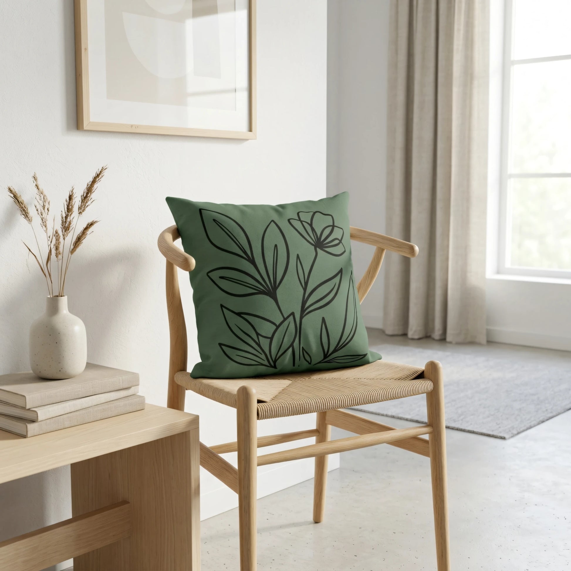 Green throw pillow with black botanical line art on a light wood chair in a bright, minimalist room featuring neutral home decor.