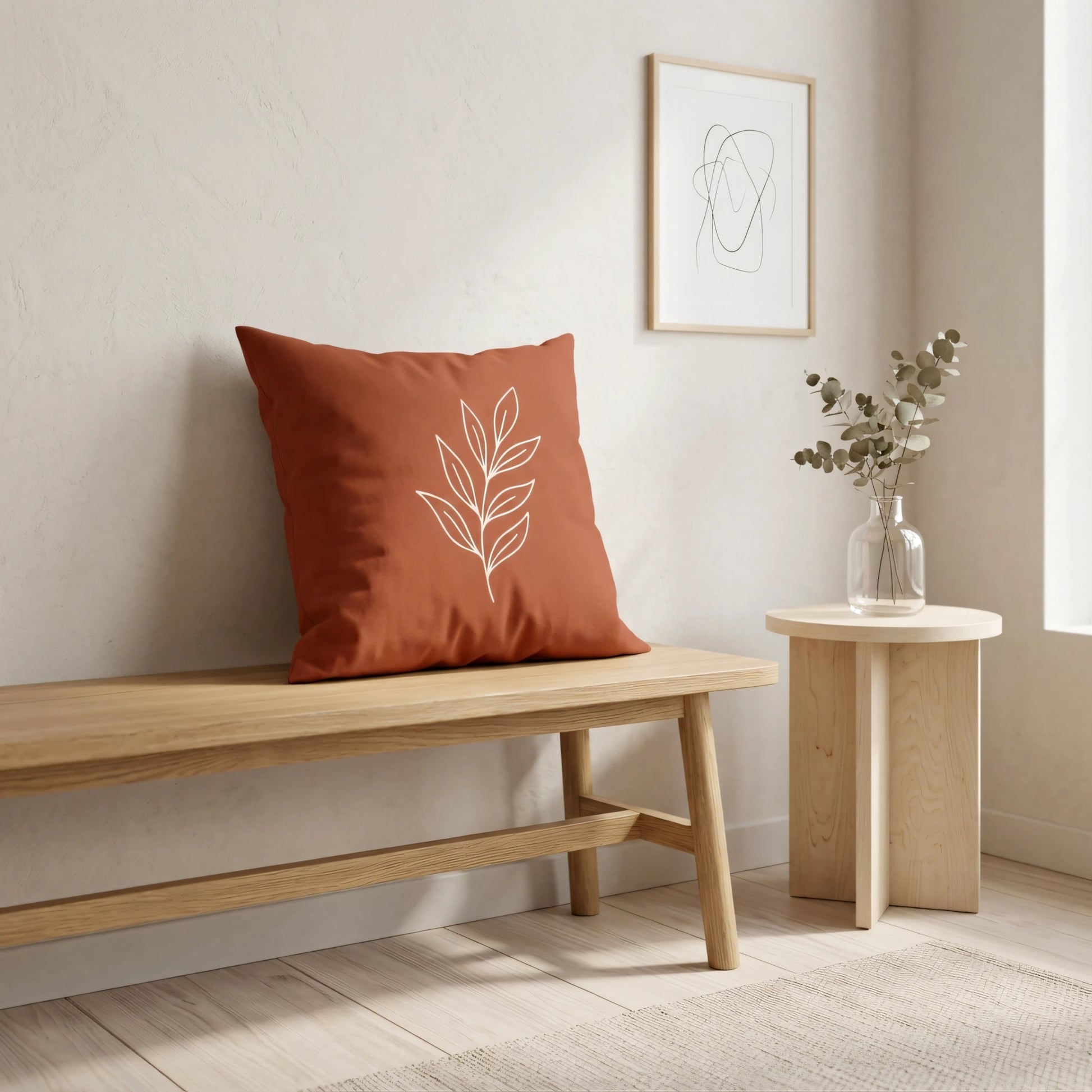 Minimalist terracotta pillow with white leaf line art on a wooden bench in a modern, neutral room with elegant decor and natural light.