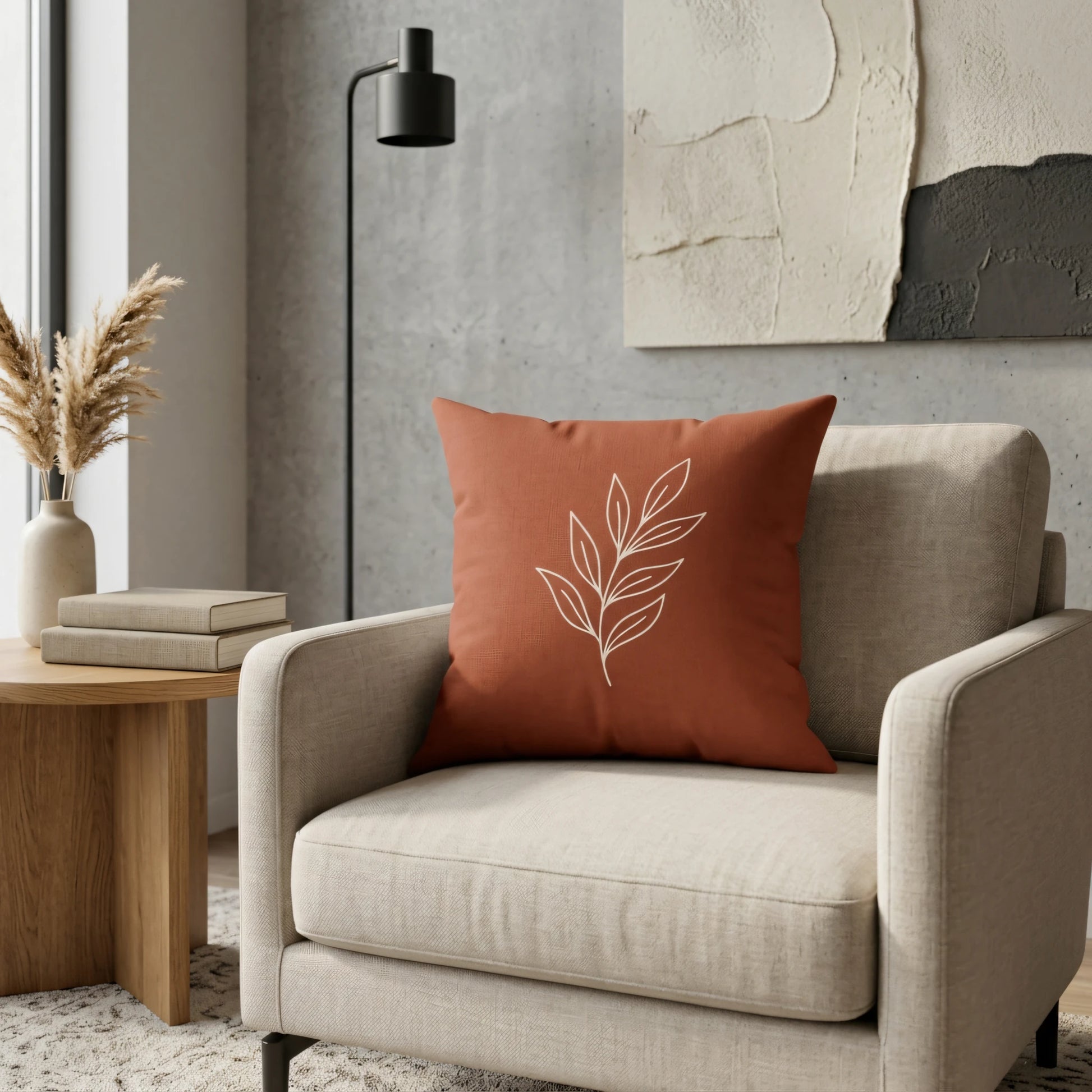 Burnt orange throw pillow with white leaf line art on a beige armchair in a modern living room with neutral decor and a minimalist side table.
