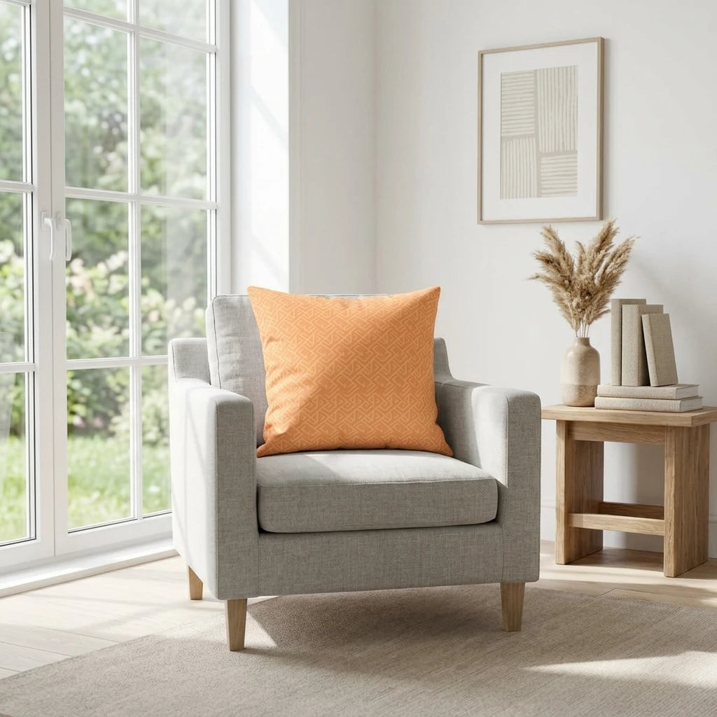 Orange geometric pattern cushion on a gray armchair in a sunlit modern living room with minimalist wooden decor and large windows.
