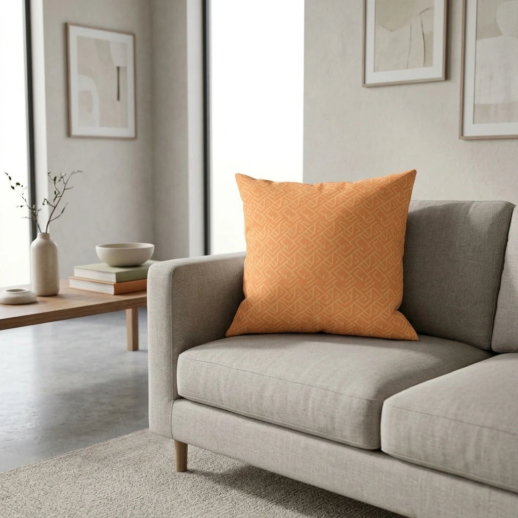 Orange geometric pattern throw pillow on a grey sofa in a modern minimalist living room setting with bright, clean decor.