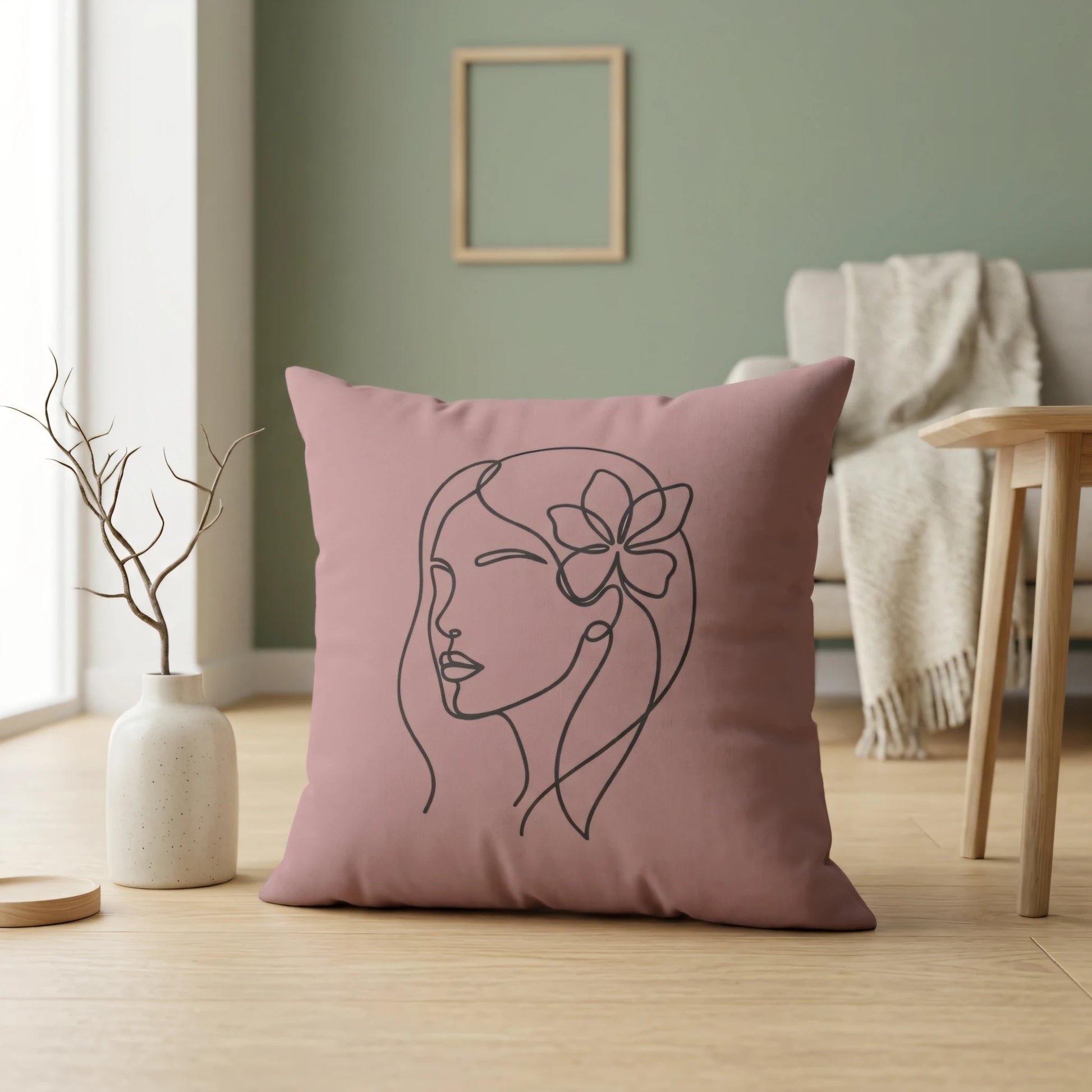 Dusty rose pillow with minimalist woman line art design in a modern interior setting with sage green walls and light wood flooring.