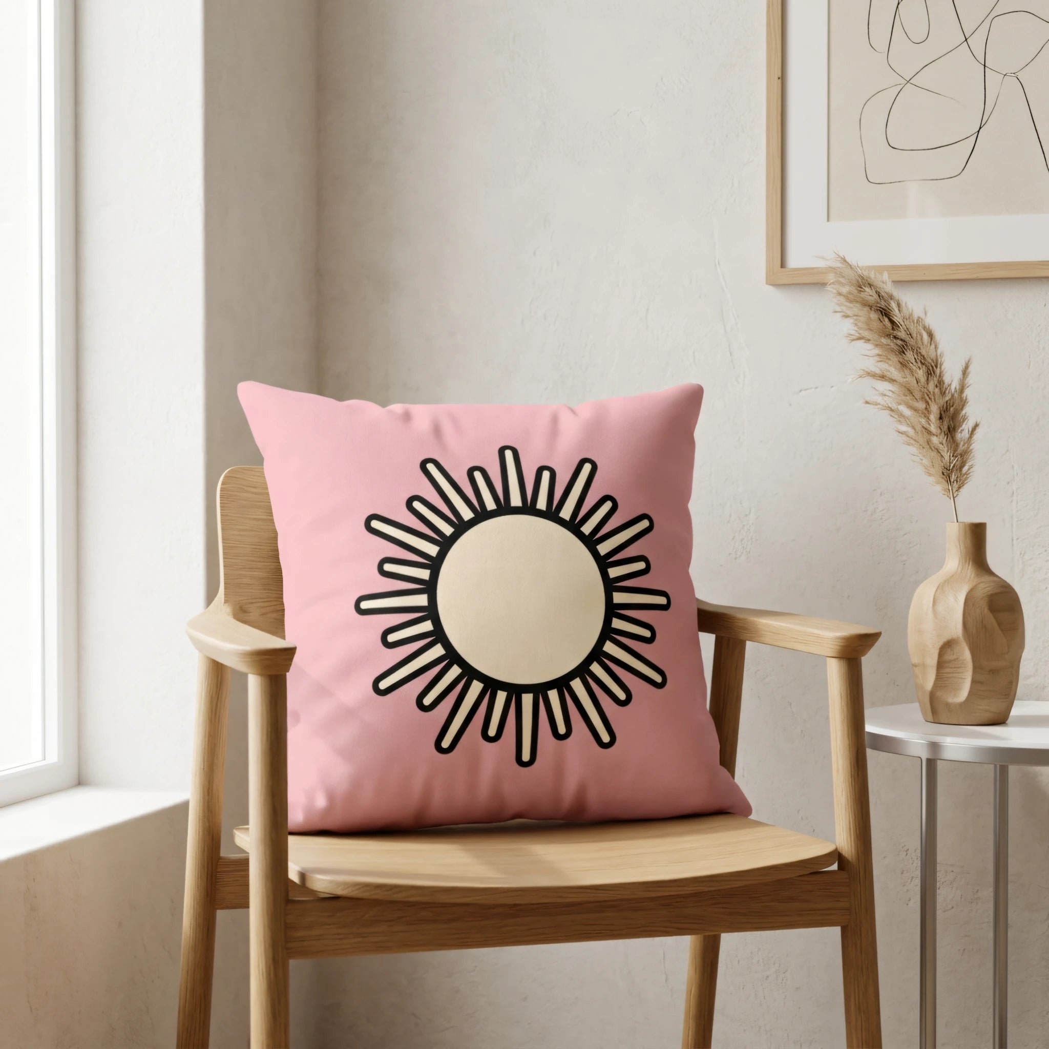 Pink cushion with a minimalist sun design on a light wood chair in a bright, modern interior setting with neutral wall decor.