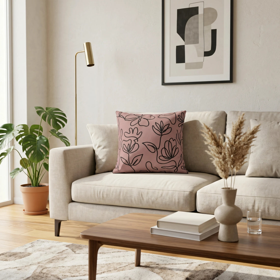 Pink floral line art cushion on a beige sofa in a modern living room setting with a monstera plant and a wooden coffee table.