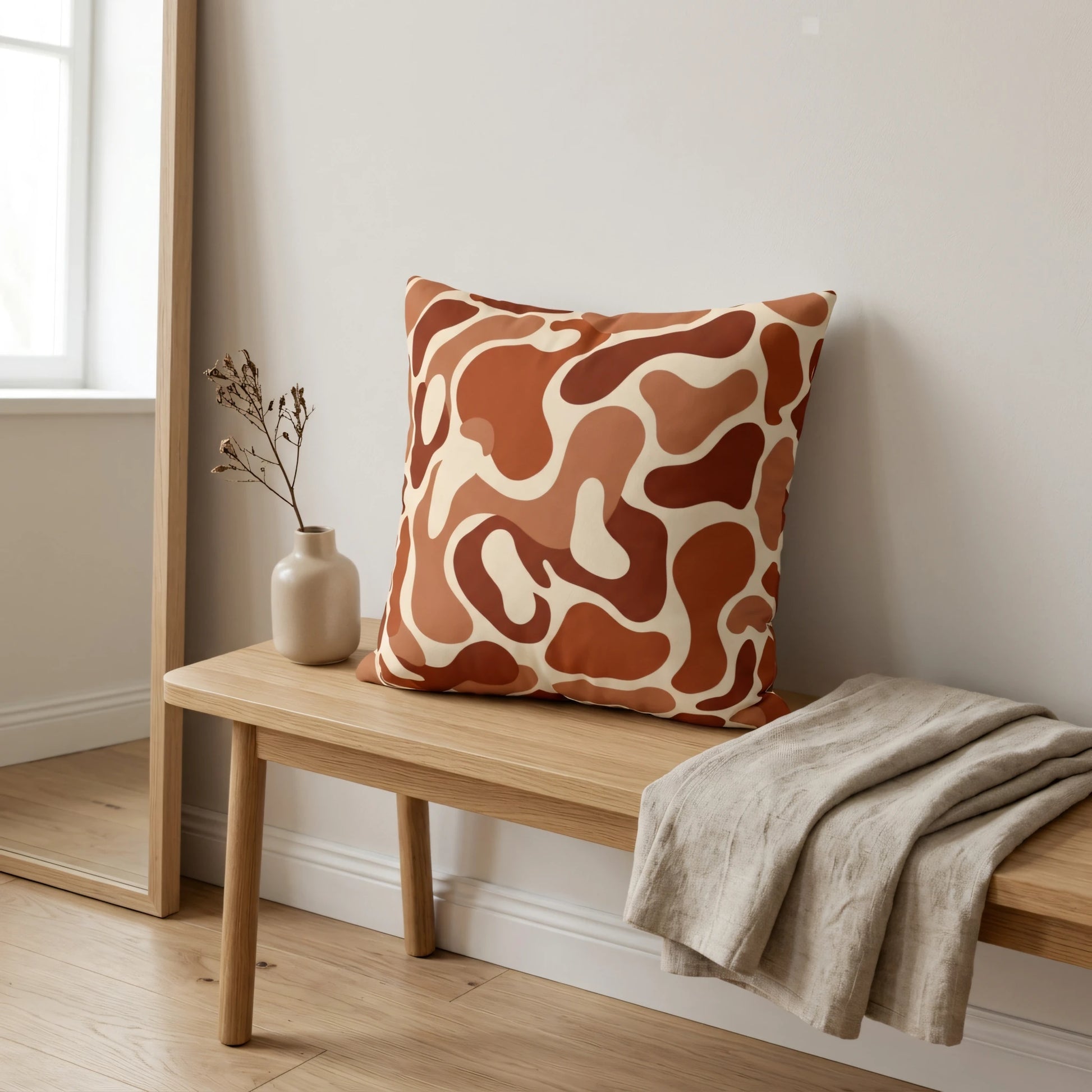 Abstract brown and terracotta pattern cushion on a wooden bench in a minimalist interior lifestyle setting with a linen throw blanket.