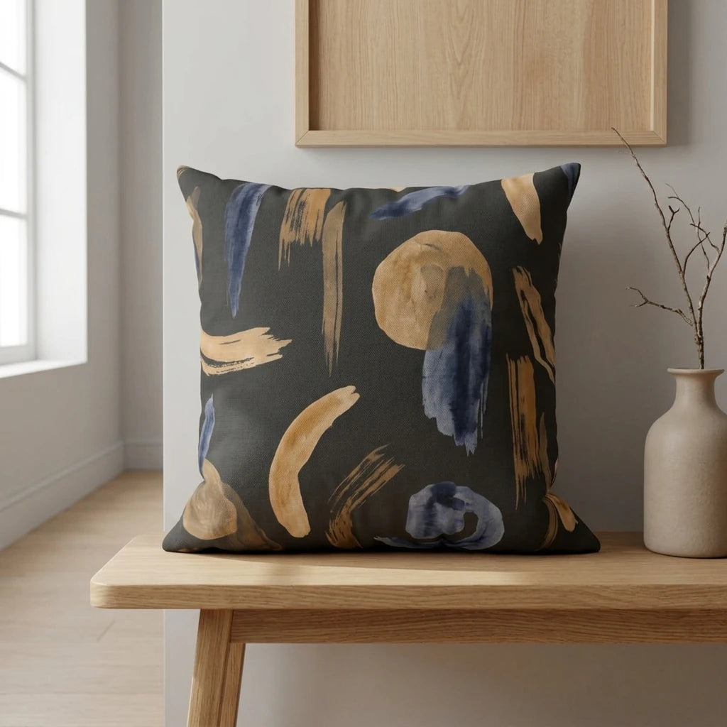 Abstract navy and ochre brushstroke pillow on a light wood bench in a minimalist interior lifestyle scene with neutral walls and natural light.