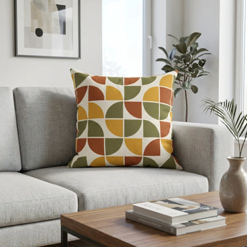 Modern geometric throw pillow with mustard, terracotta, and olive patterns on a grey sofa in a bright living room scene.