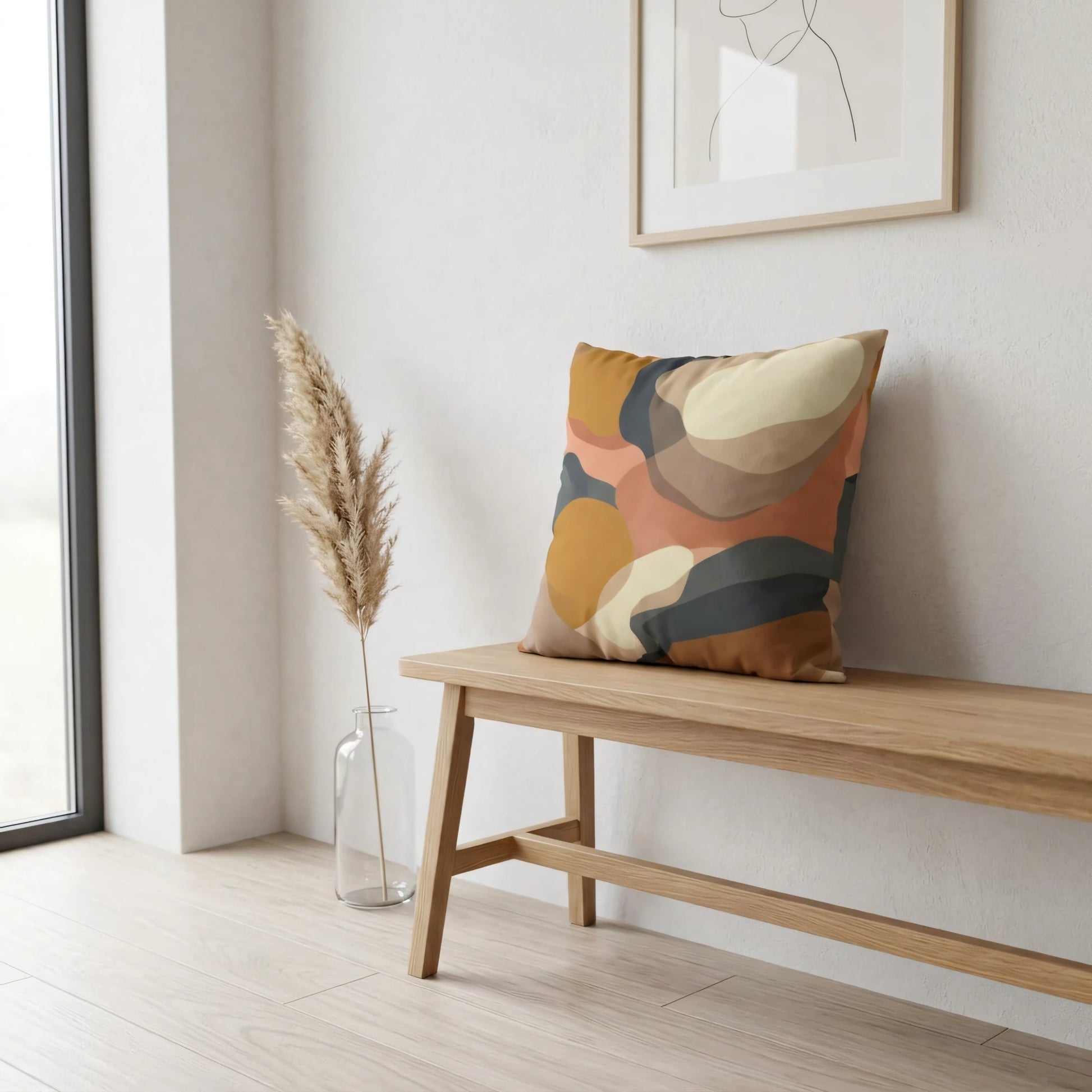 Abstract cushion with earth-toned organic shapes on a wooden bench in a minimalist room with pampas grass and line art decor.